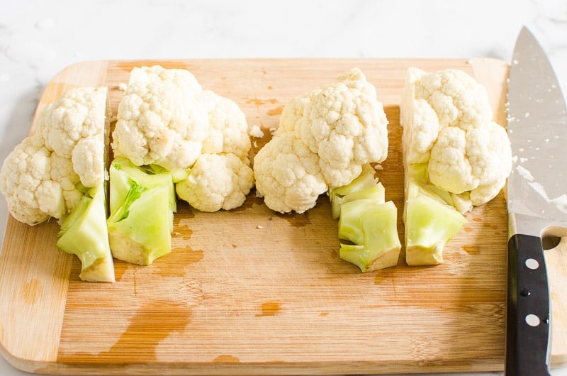 Cut cauliflower into four quarters on a cutting board with a knife.