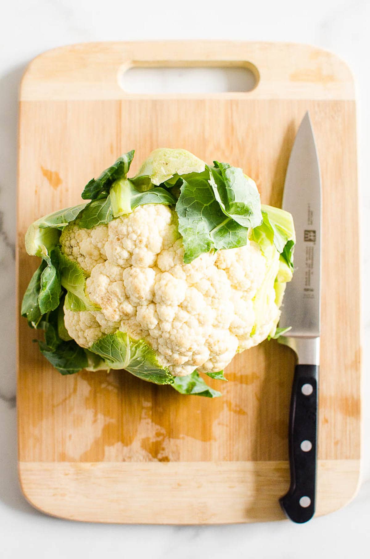 A head of cauliflower on cutting board with knife.