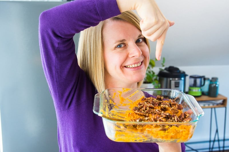 olena holding Instant Pot Sweet Potato Casserole in a glass dish and pointing with a finger at it