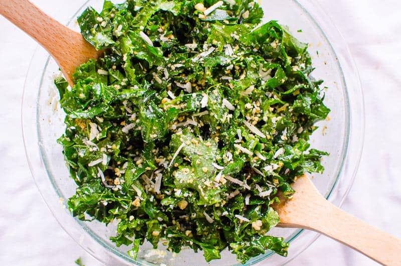 Kale salad with lemon, garlic and parmesan in a bowl with serving utensils.