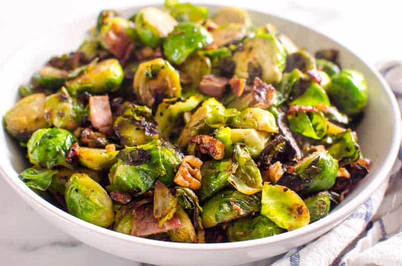 Sauteed brussels sprouts with bacon and pecan in white bowl.