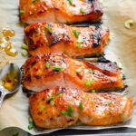 Thai sweet chili salmon with sweet chili sauce on parchment lined baking sheet.