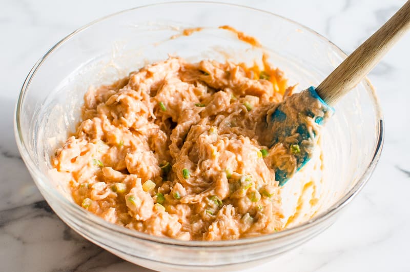 Healthy buffalo chicken dip in glass bowl stirred with spatula. 