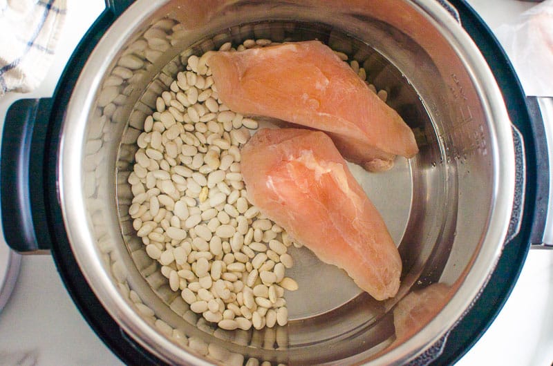 Two chicken breasts, fried white beans and water in Instant Pot. 