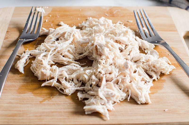 Shredded cooked chicken breasts with two forks on a cutting board. 