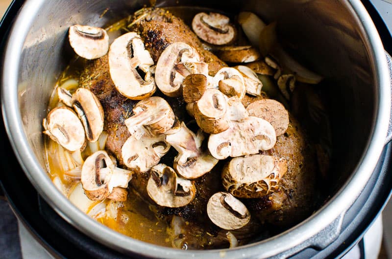 Mushrooms on top of a roast and onions in broth inside the pot.