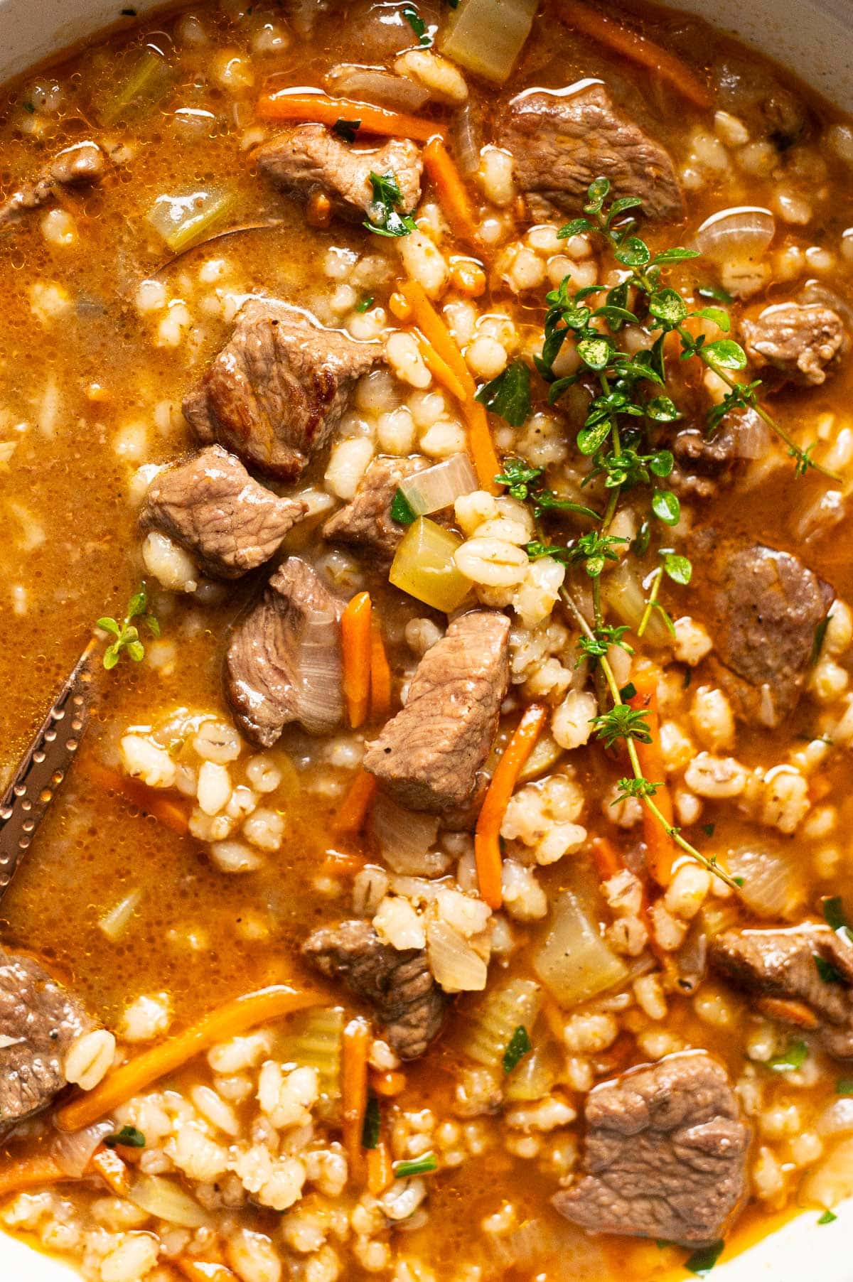 Beef barley soup garnished with thyme in a bowl.