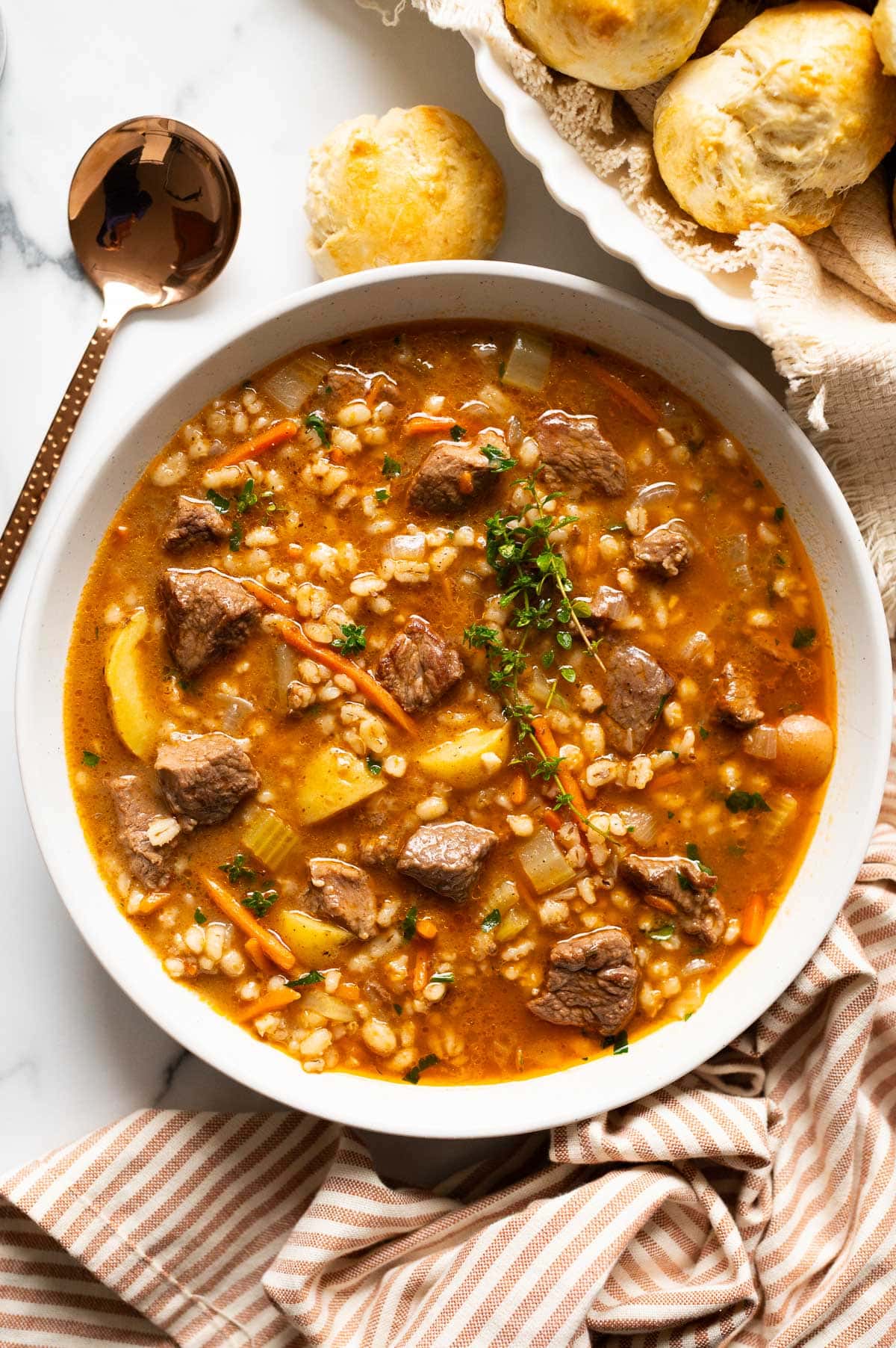 Beef barley soup served with dinner rolls.