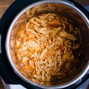 Instant Pot BBQ chicken breast that is shredded in pressure cooker liner.