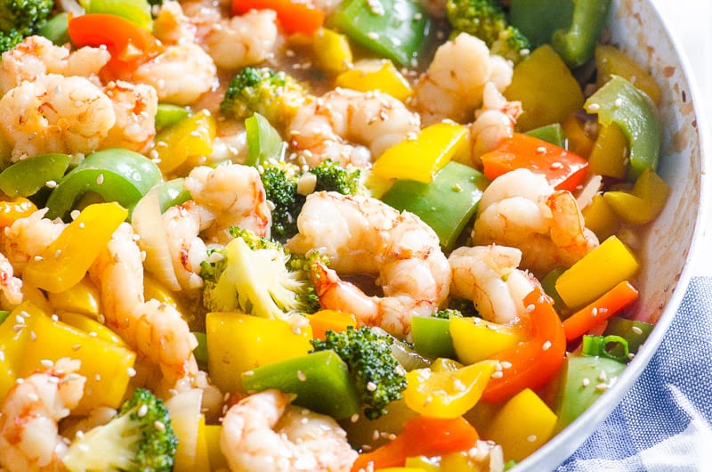 Shrimp, broccoli, peppers garnished with sesame seeds in skillet.