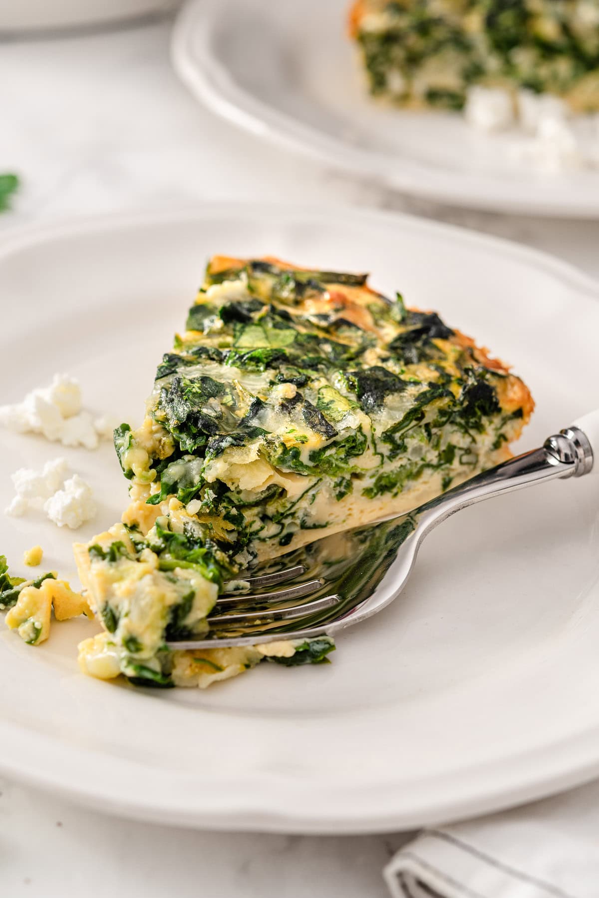 A slice of crustless spinach quiche served on a plate with a fork.