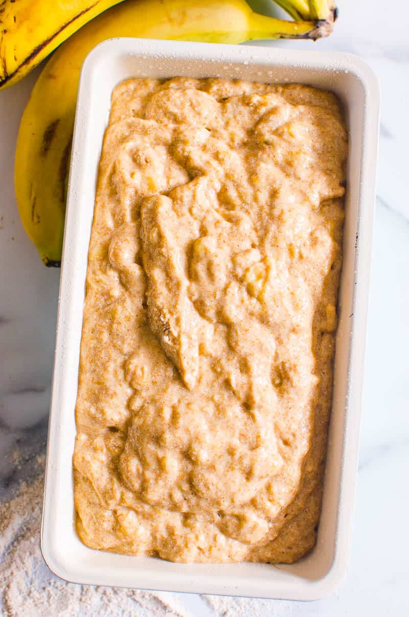 Unbaked banana bread in a loaf tin and bananas nearby.