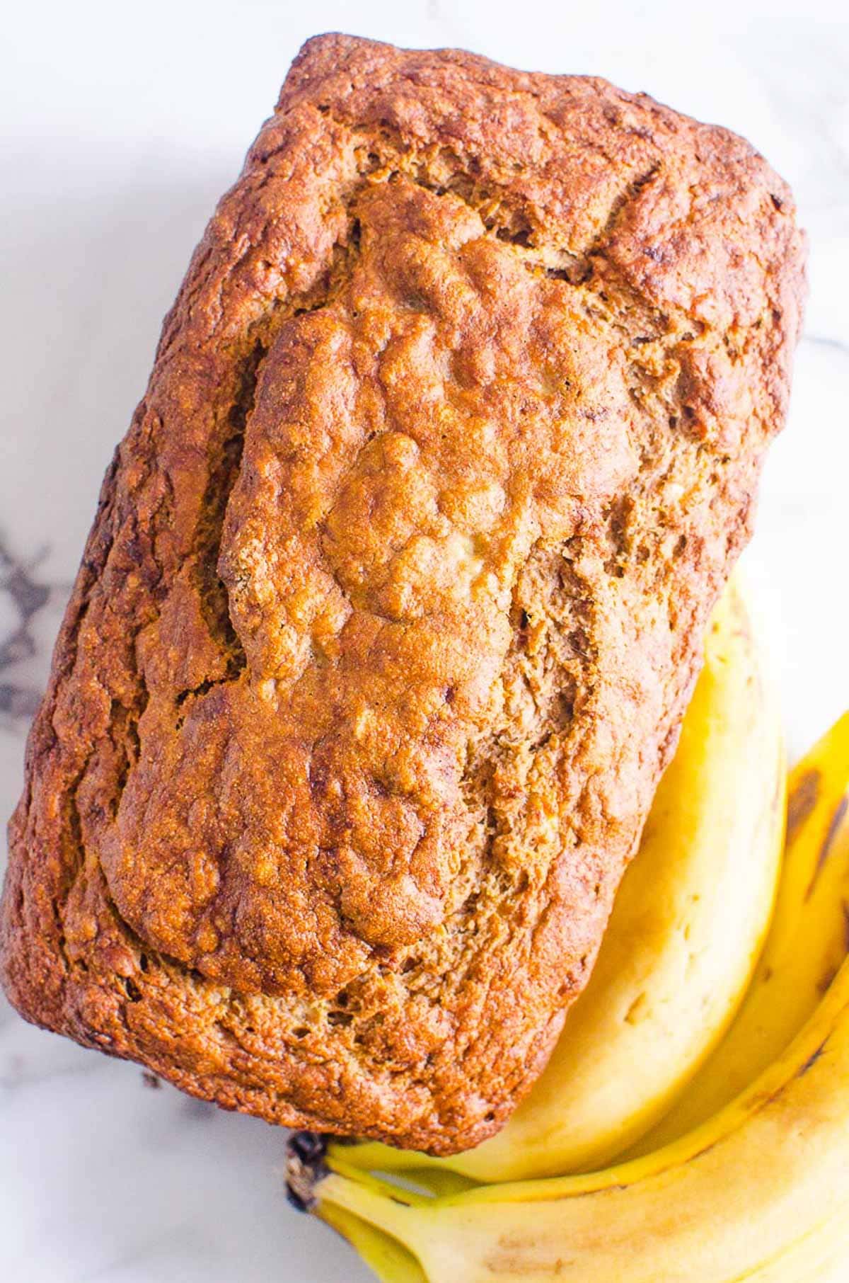 Healthy banana bread on a counter with bananas nearby.
