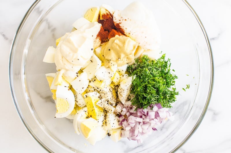 chopped eggs, red onion, dill, spices, mayo and yogurt in glass bowl
