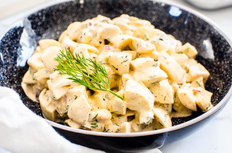 Healthy egg salad served in a black bowl with dill garnish.