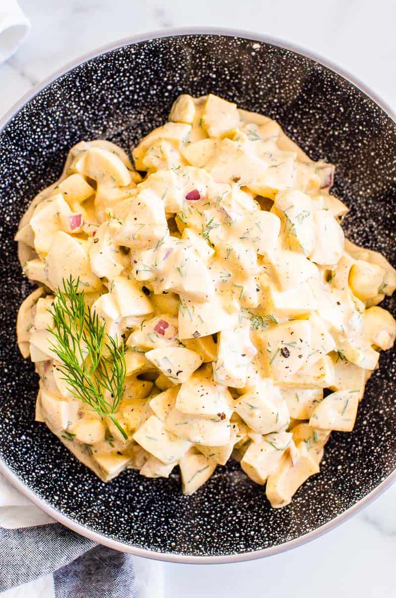 Healthy egg salad with dill garnish in black bowl.