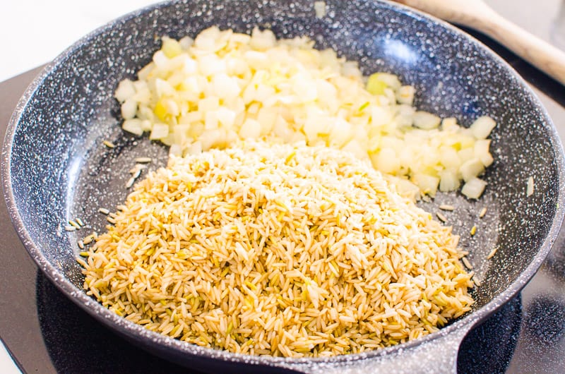A pile of onion on one side and brown rice on the other side of the skillet. 