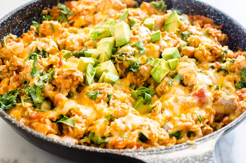 Mexican Chicken and Rice in a skillet with melted cheese and diced avocado on top.