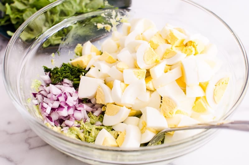 Avocado Egg Salad ingredients in a bowl include eggs, red onion, dill and avocado