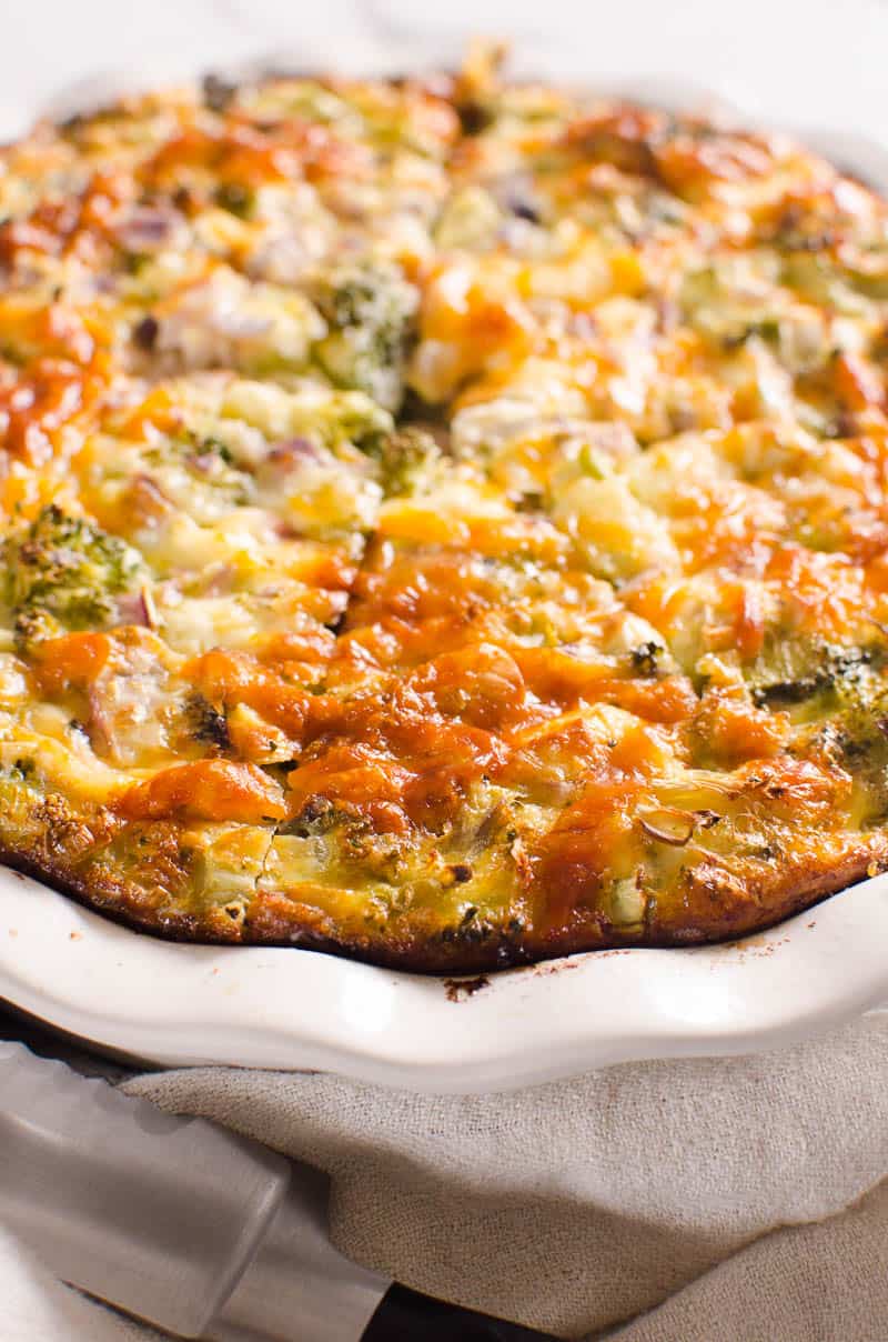 Crustless Broccoli Quiche recipe sliced in a pie dish, knife and towel 