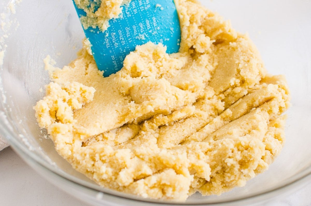 Blue spatula with almond flour cookie dough batter in bowl.