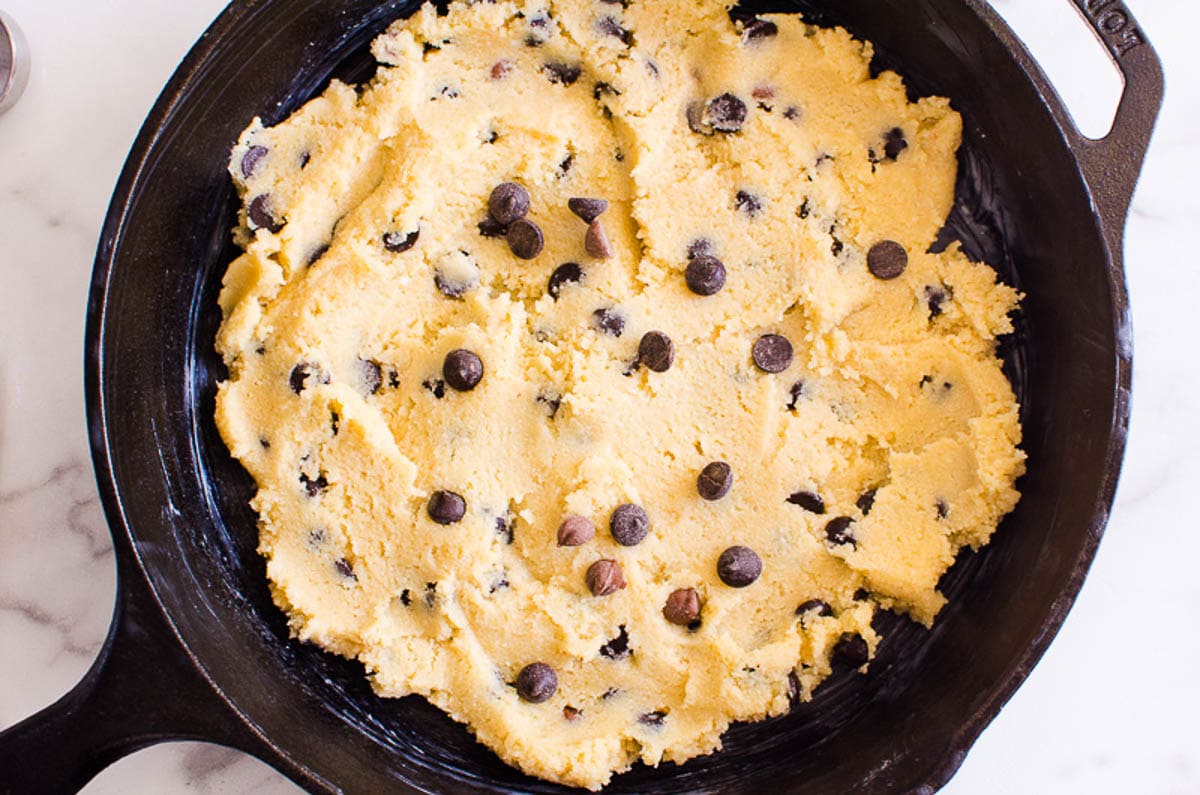 Chocolate chip cookie dough flattened in cast iron skillet. 