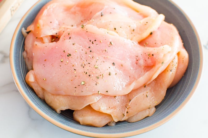 Chicken cutlets sprinkled with salt and pepper in a bowl.