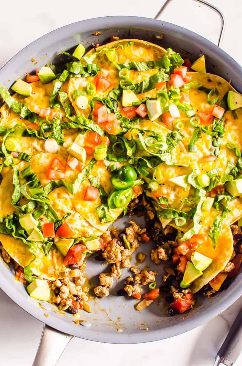 Looking down on a taco skillet garnished with lettuce, jalapeno, green onion and avocado.