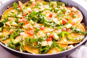 Lettuce and tomatoes on top of corn tortillas with cheese in a skillet. 