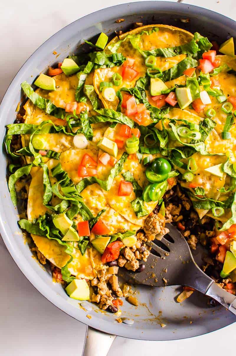 Taco skillet garnished with jalapeno, avocado and tomatoes and spatula in it.