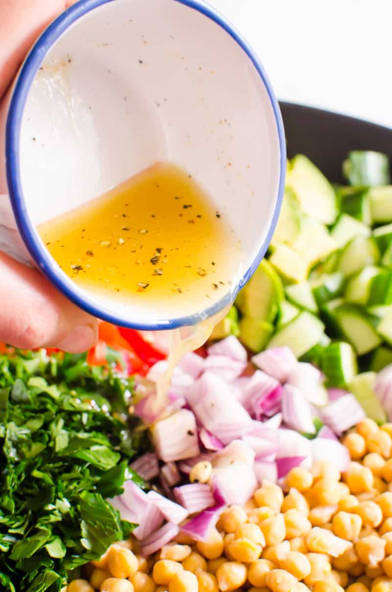 Pouring dressing over salad in bowl.