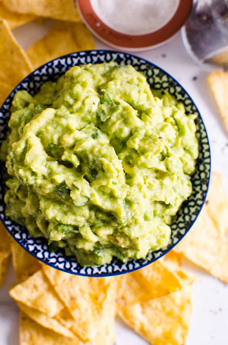 Guacamole in blue bowl served with chips and salt and pepper shaker nearby.