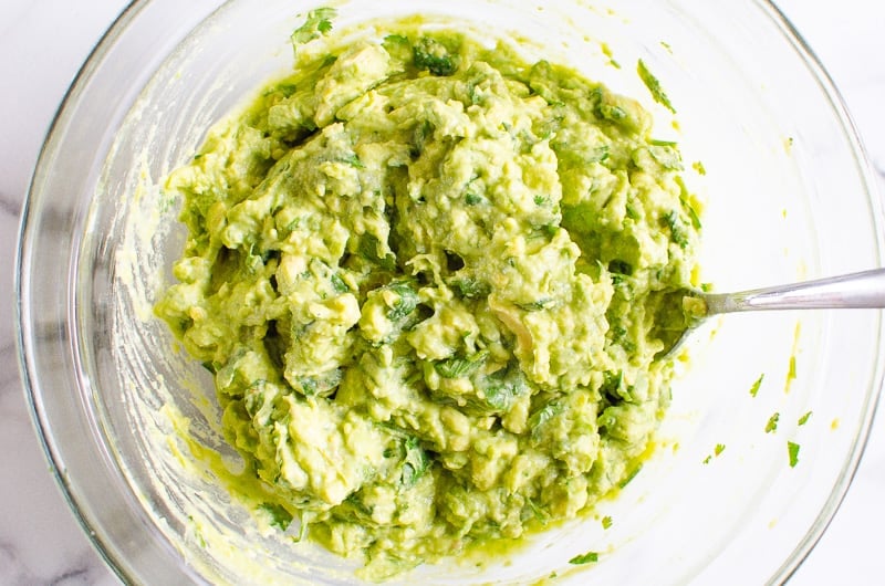 Combined guac in glass bowl with a fork.