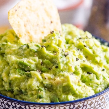 A chip dipped in the guacamole in blue bowl.