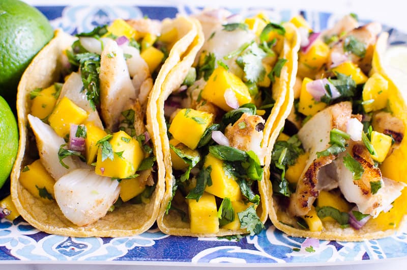 Three grilled fish tacos with fresh mango and cilantro.