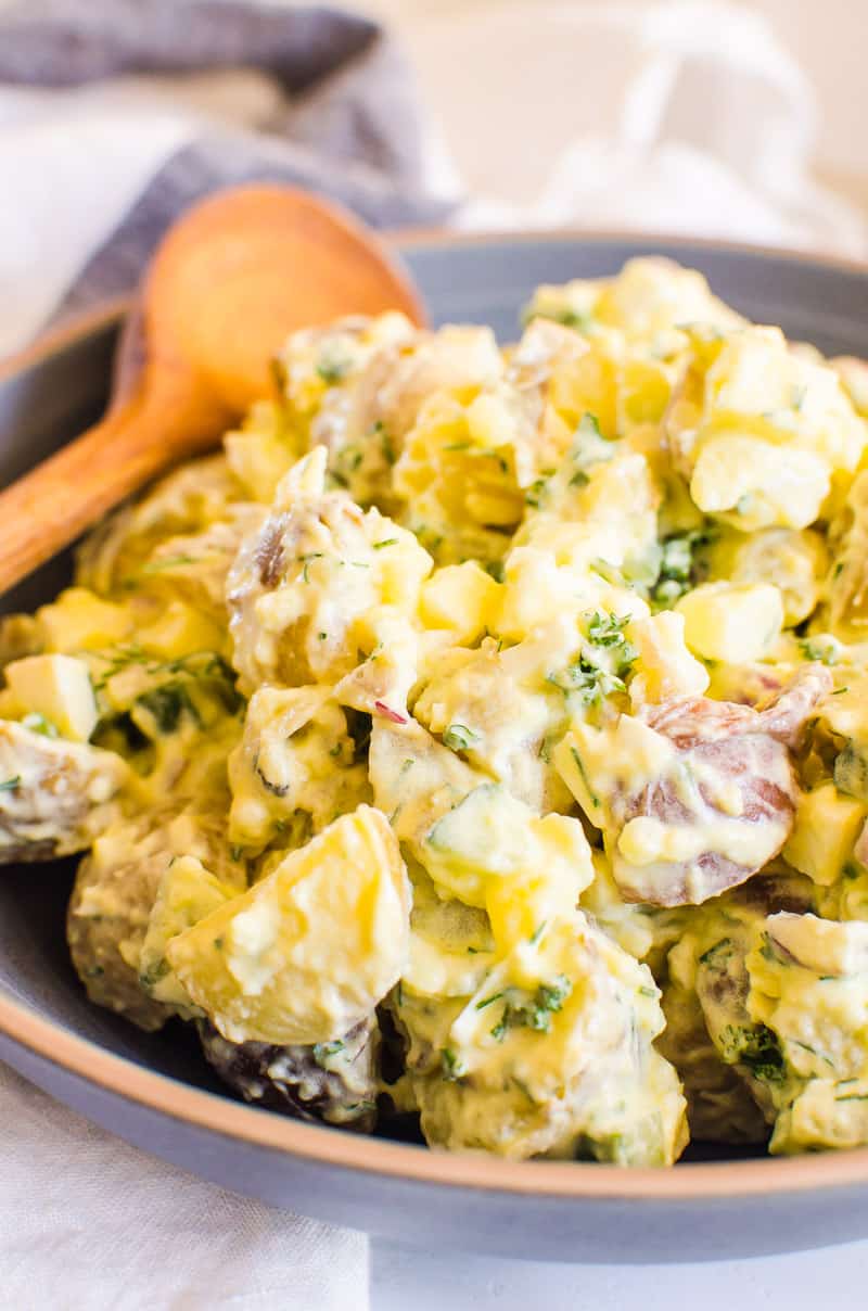 Healthy potato salad recipe served in a blue bowl with wooden spoon.