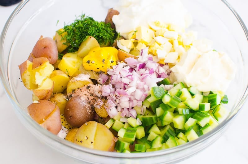 Cooked baby potatoes, eggs, cucumber, red onion, mayo, yogurt, mustard, dill, salt and pepper in a large bowl.