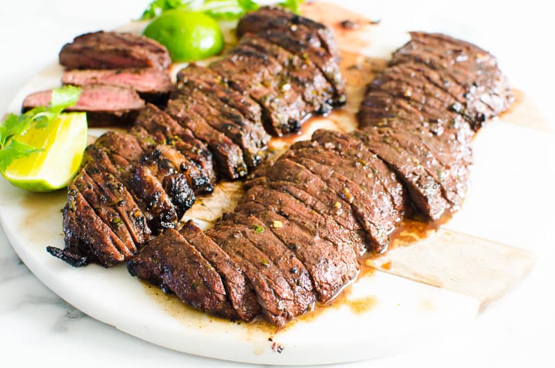 Carne asada steak sliced on cutting board with limes.