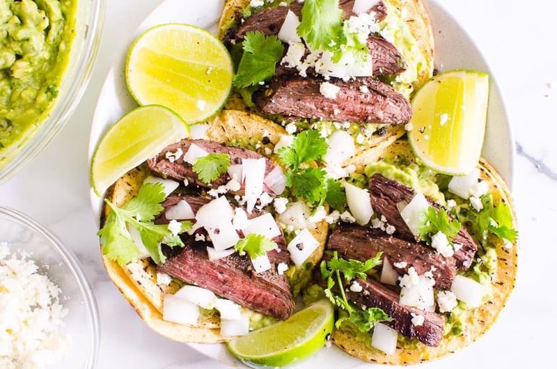 Three carne asada steak tacos served with lime, cilantro, cheese and guacamole.