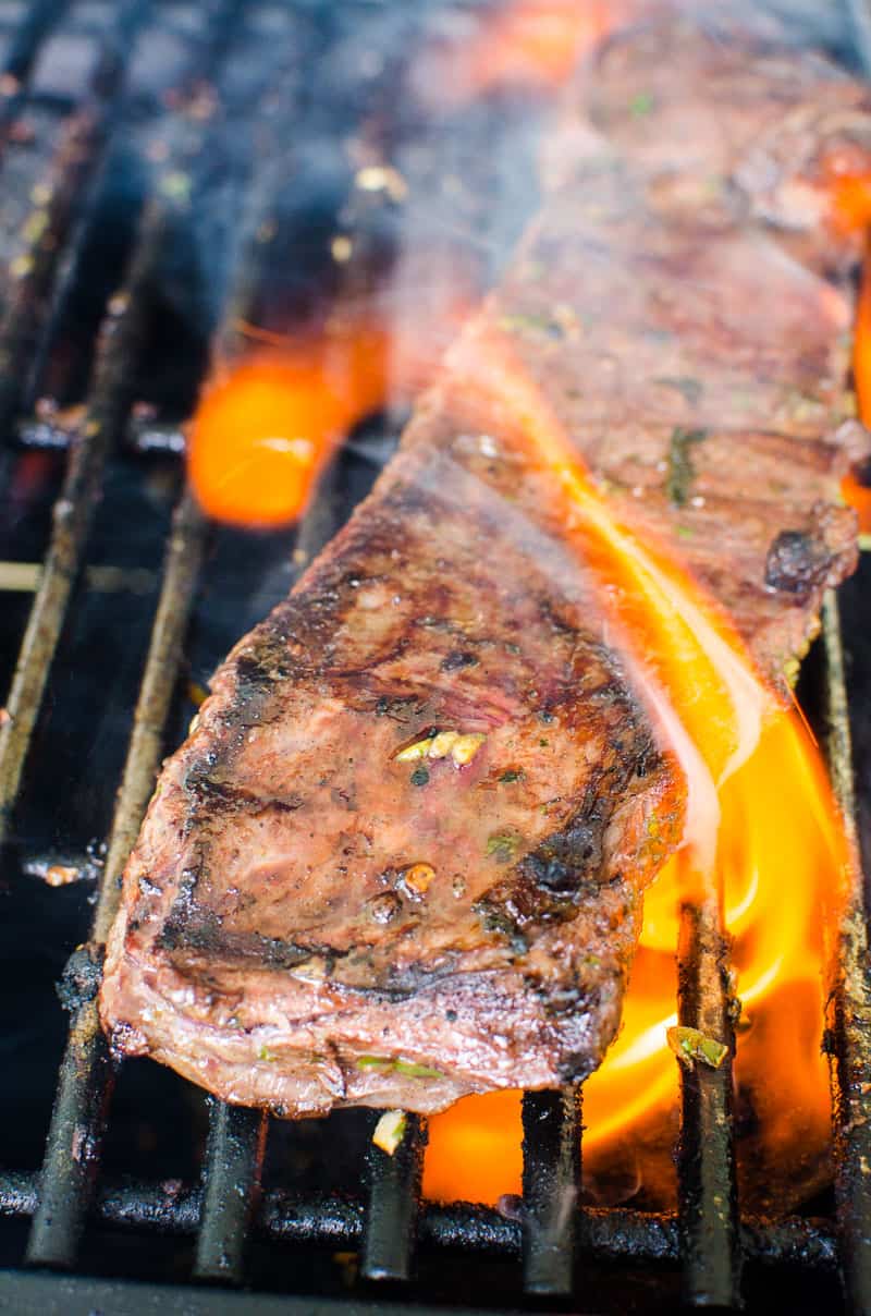 Carne asada steak on the grill with flame up.