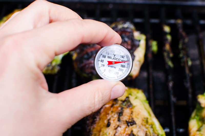 Thermometer inserted in grilled chicken thighs showing 165 degrees F.