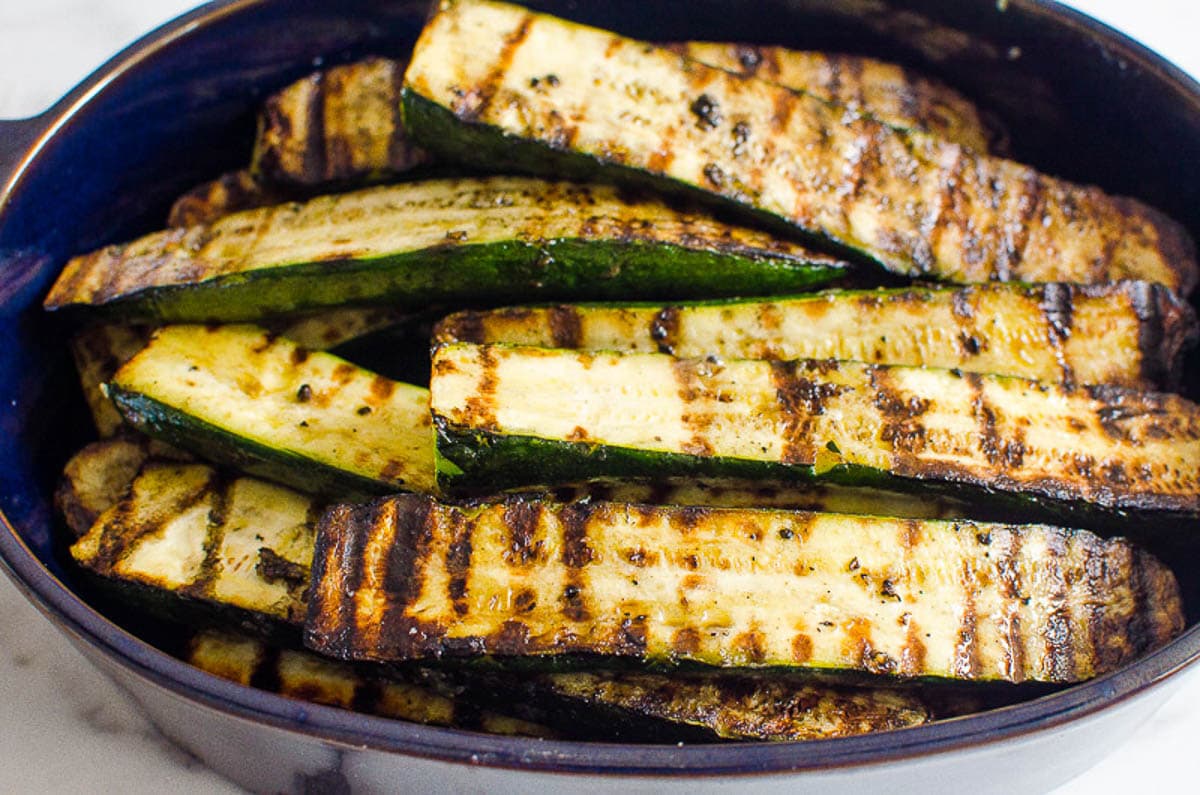 Grilled baby zucchini halves served in blue baking dish.