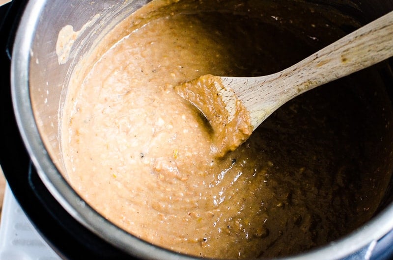 pureed Instant Pot Refried Beans with wooden spoon inside the pot