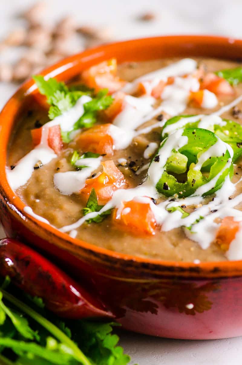 Instant Pot Refried Beans garnished with crema and sliced jalapenos and diced tomatoes