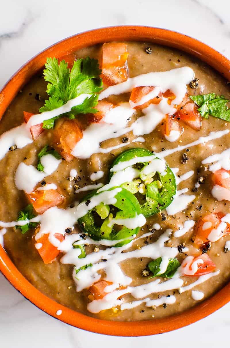 Instant Pot refried beans garnished with sour cream, jalapeno, tomato and cilantro in red bowl