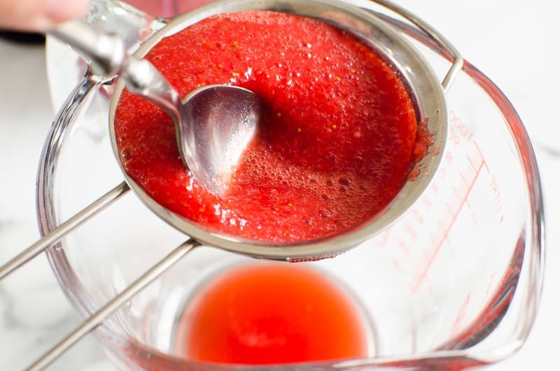 Pushing strawberry puree through a mesh strainer into measuring cup.