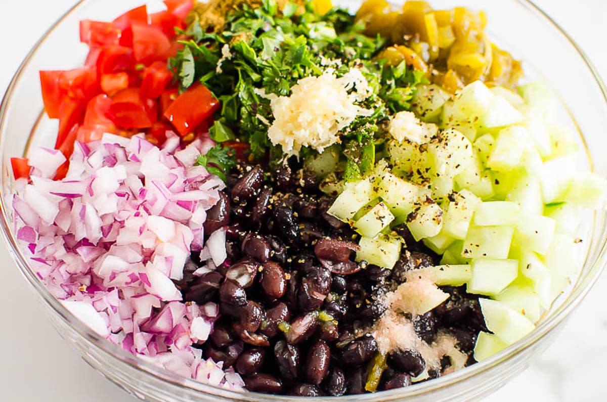 Diced cucumbers, red onion, tomatoes, green chilies, cilantro, garlic and spices in bowl.