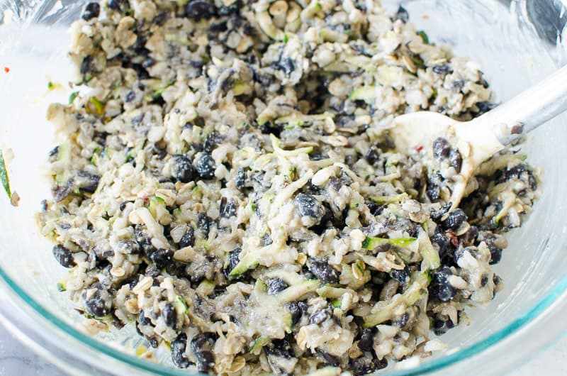 black beans, rice, eggs, zucchini and spices mixed in a glass bowl with wooden spoon