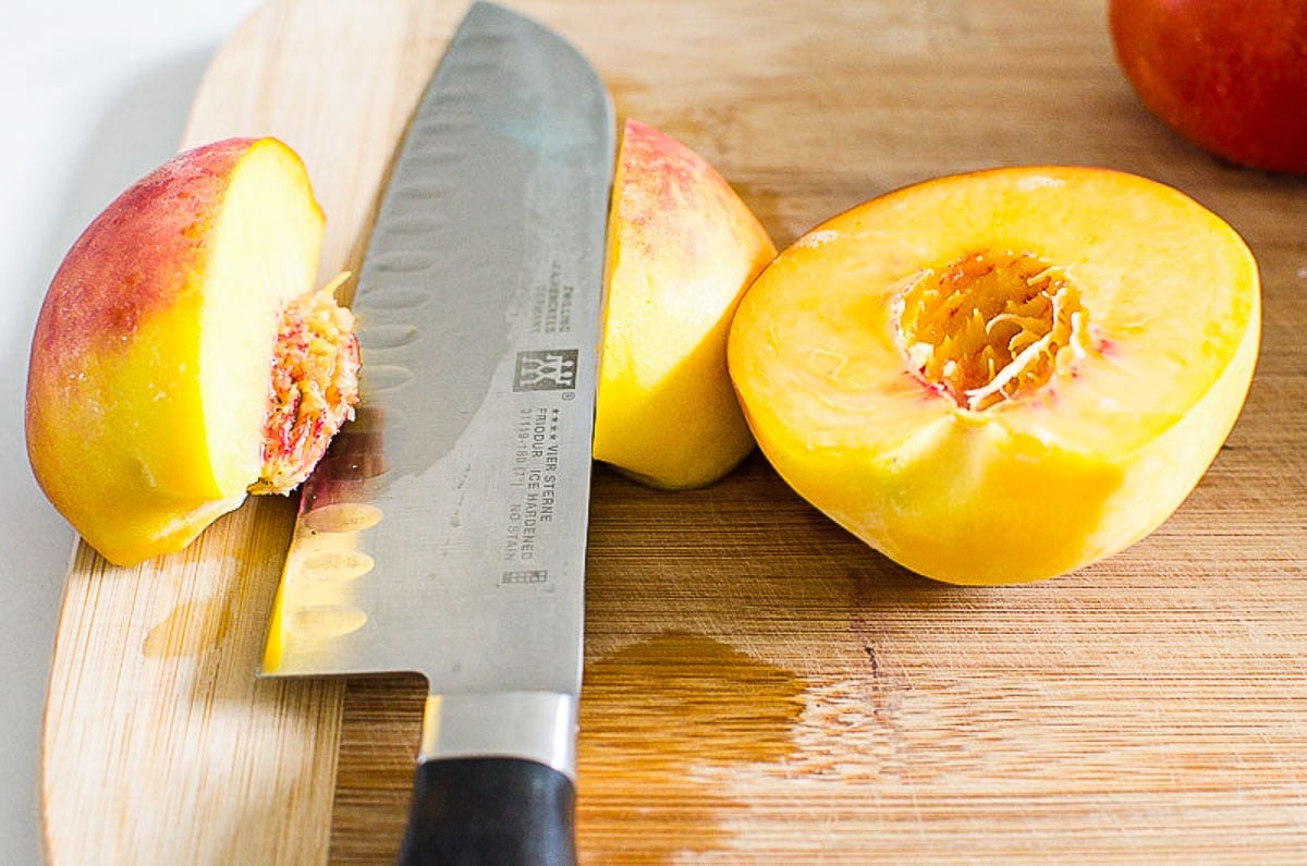 Peach cut in quarters with a knife on a cutting board.