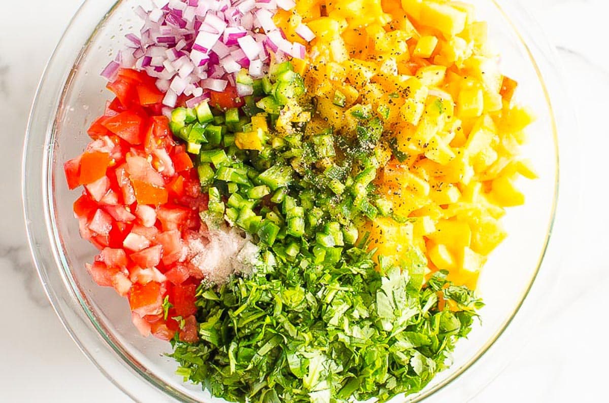 Diced tomato, peaches, red onion, jalapeno, cilantro and spices in glass bowl.